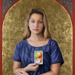 A woman holding up a tarot card in front of a gold background.